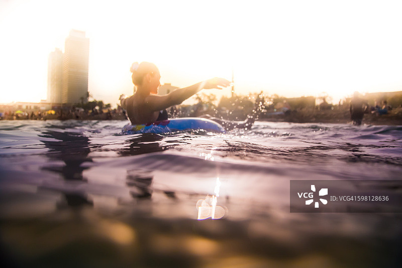女孩游泳在地中海充气环垫与巴塞罗那城市的天际线在夏季日落时间没有压力和放松的时间。图片素材