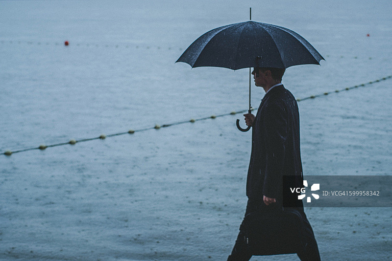 帅气的男人穿着西装，在雨中撑着伞图片素材