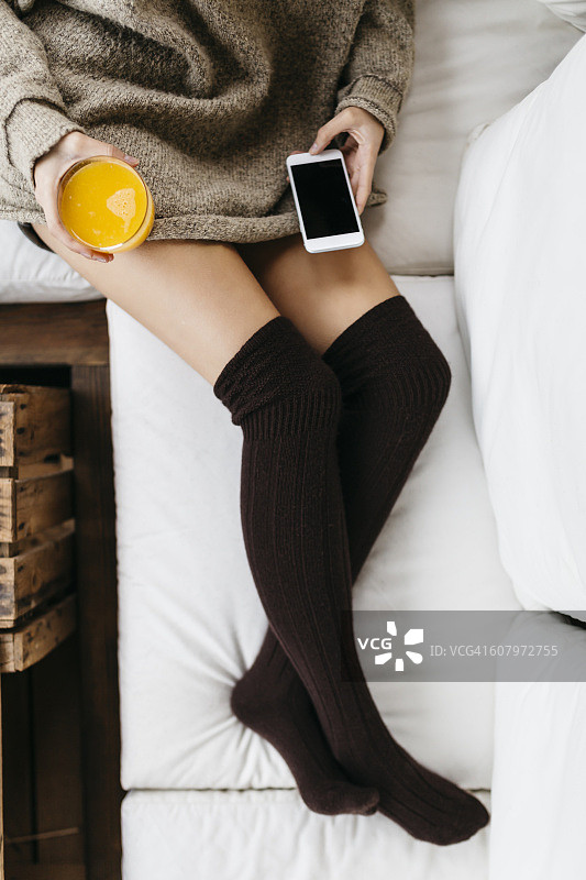 女人用智能手机和一杯橙汁放松图片素材