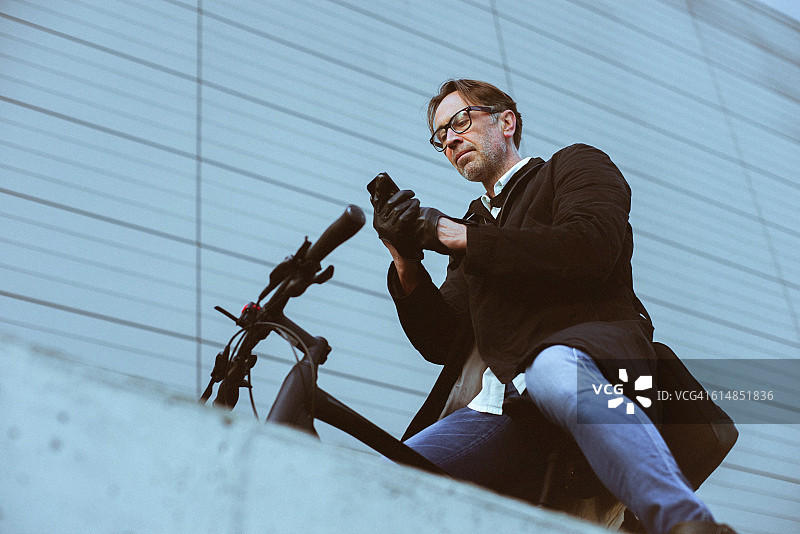 帅哥骑着自行车在现代建筑旁边用智能手机图片素材