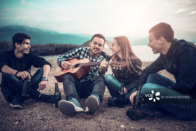 四个面带微笑的人拿着原声吉他在海滩露营时唱歌图片素材