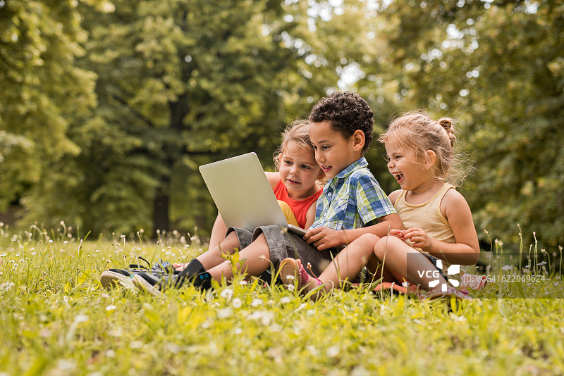 小快乐的朋友们在公园的草地上使用笔记本电脑。图片素材