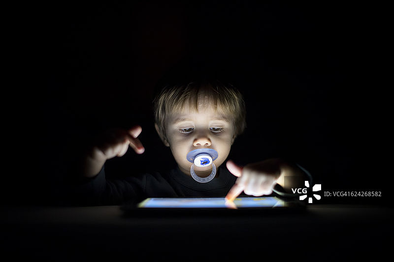 1岁的小男孩在黑暗中寻找数码平板电脑图片素材