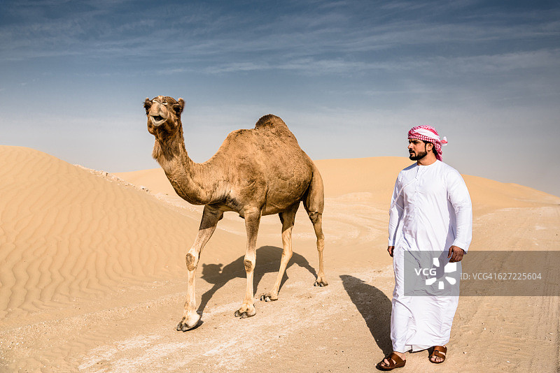 阿拉伯酋长在沙漠里和骆驼一起行走图片素材