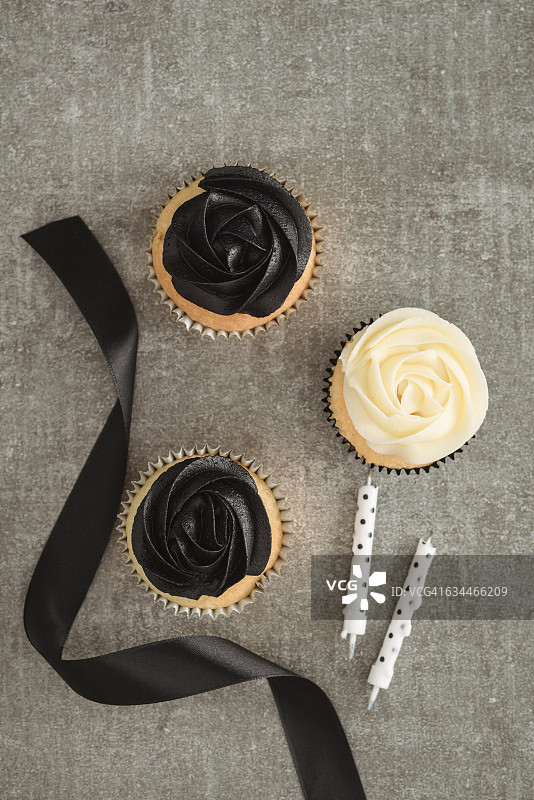 杯型蛋糕，上面有黑色和奶油色的奶油，缎带和两支蜡烛图片素材