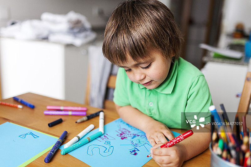 小男孩在家里用蓝色的纸画画图片素材