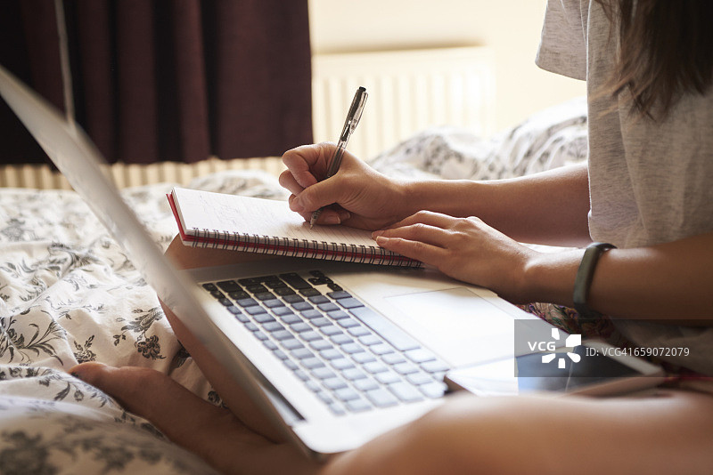 一个女人坐在床上使用笔记本电脑的特写图片素材