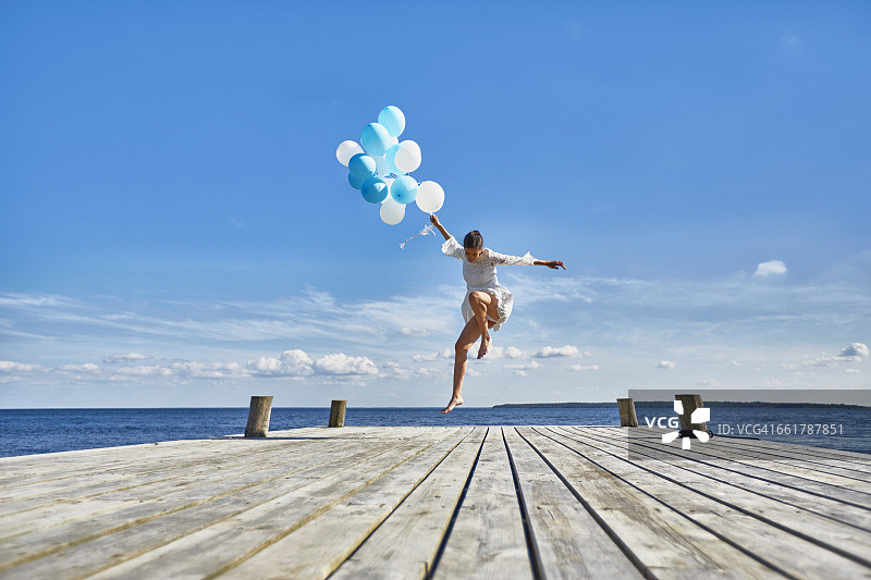 年轻女子在木码头上跳舞，手里拿着一串气球图片素材