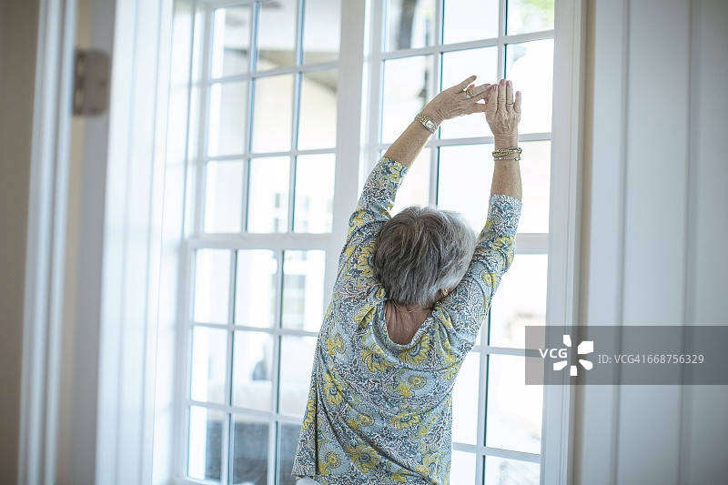 年长的女人在窗前伸懒腰图片素材