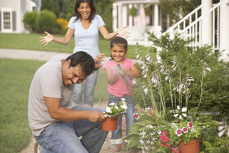 西班牙家庭在花园里浇水，在户外玩水龙带图片素材