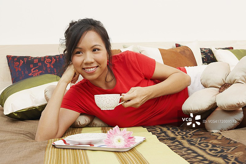 一个年轻女人的特写躺在床上，拿着一杯茶图片素材
