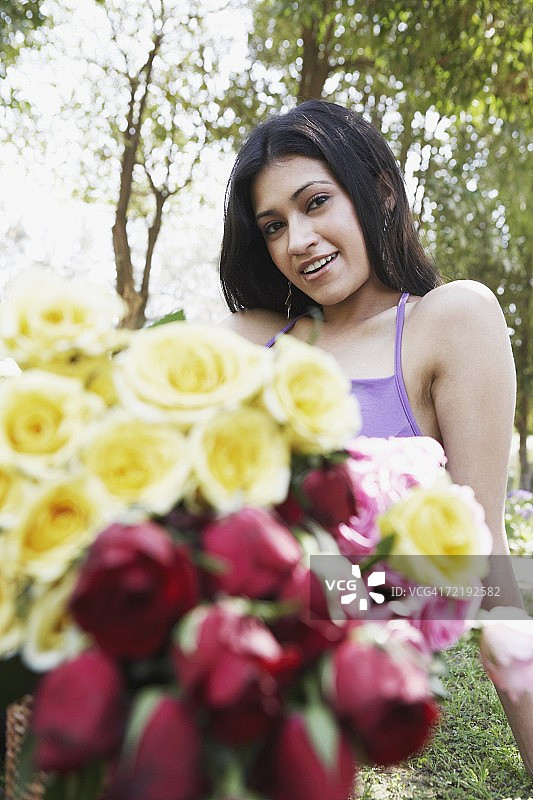 一个年轻女子坐在公园里捧着一束玫瑰花的肖像图片素材