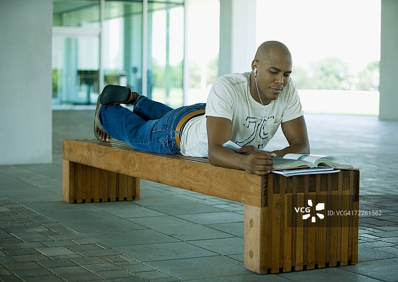 男学生一边学习一边听耳机，躺在长凳上图片素材