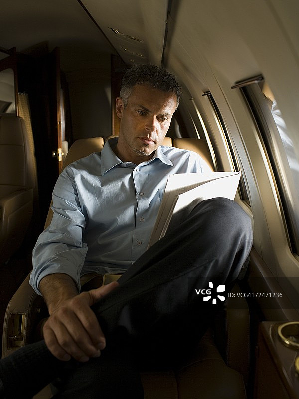 一个商人在飞机上看报纸图片素材