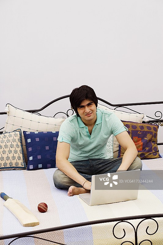 一个年轻人在床上用笔记本电脑的肖像图片素材