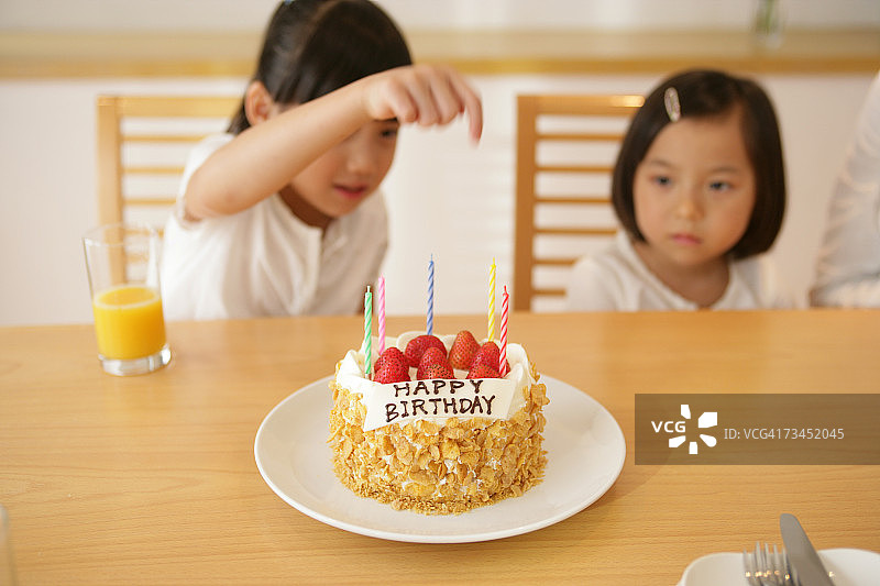 女孩和她的妹妹坐在桌前，面前放着一个生日蛋糕图片素材