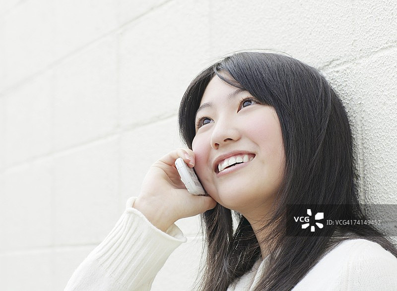 日本年轻女子在墙边用手机说话图片素材