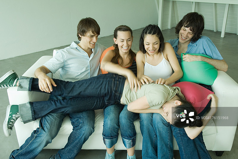 "一群年轻人坐在沙发上，一个躺在别人的腿上"图片素材