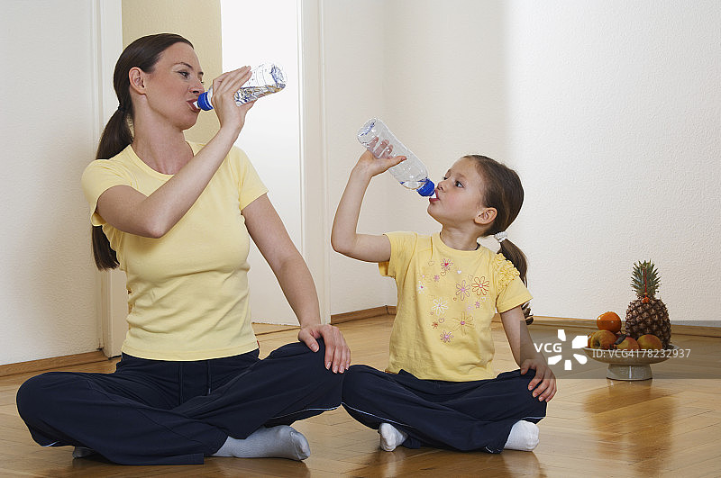 母亲和女儿一起坐在地板上喝着塑料瓶里的水图片素材