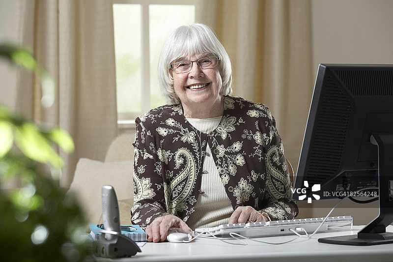 微笑的老妇人坐在电脑前图片素材