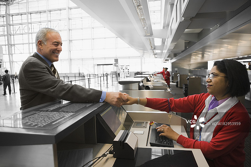 一个商人微笑着和航空公司的值机人员握手的侧面照片图片素材