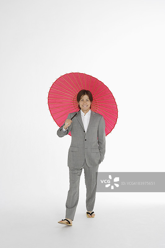 一名商人穿着日本凉鞋，拿着日本伞，在摄影棚拍摄图片素材