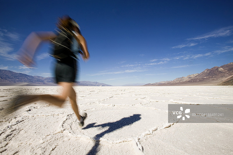 美国犹他州博纳维尔盐滩，妇女在龟裂的沙漠景观中奔跑图片素材