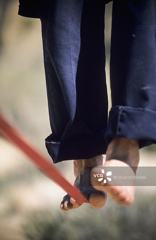 一个男人的光脚平衡在一根绷紧的绳子或在加利福尼亚沙漠松弛的绳子上的特写。图片素材