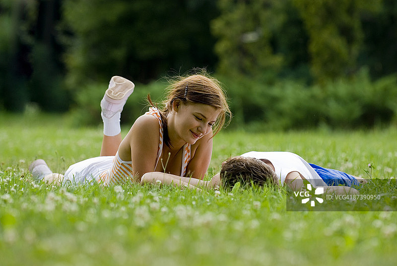 一对年轻夫妇躺在公园的草坪上调情图片素材