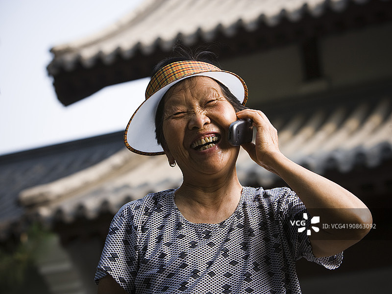 老妇人在户外用遮阳板微笑着打电话图片素材