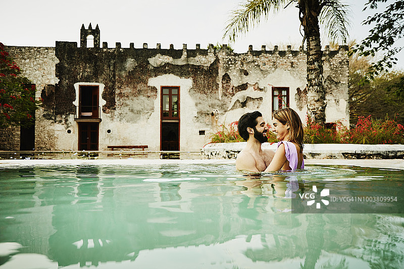 微笑的夫妇拥抱，而放松在豪华的热带度假泳池图片素材