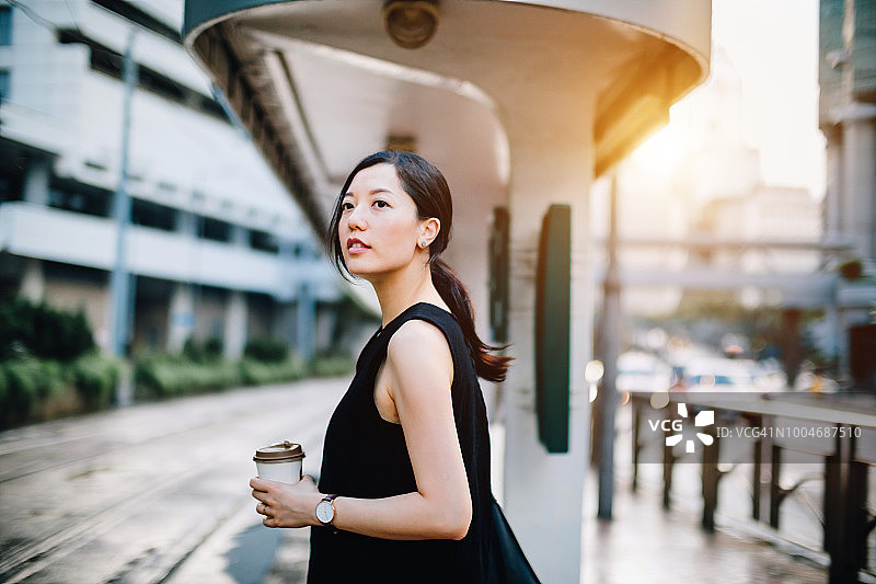 美丽的年轻女士拿着咖啡杯在城市的车站等电车图片素材