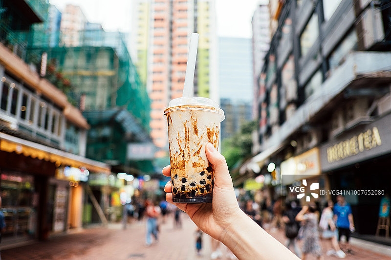 在一个炎热的夏天，人们拿着一瓶冰凉的珍珠奶茶走在城市的街道上图片素材