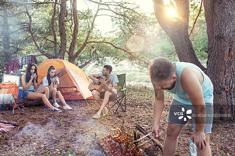聚会，男女团体露营在森林。他们放松，唱歌，做烧烤图片素材