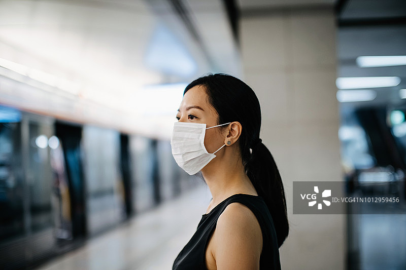 一名亚洲妇女戴着防护口罩在月台等候地铁列车图片素材