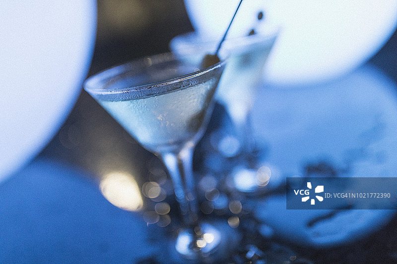 在拿骚的夜晚，在蓝色的灯光下，两杯脏兮兮的马提尼酒，橄榄放在冰块中间。图片素材