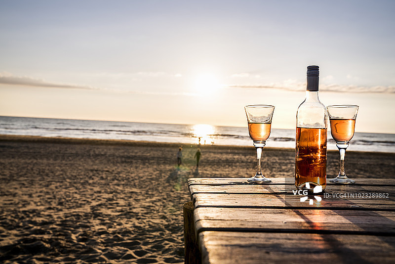 日落时分，海滩木板路上的酒瓶和玻璃杯图片素材