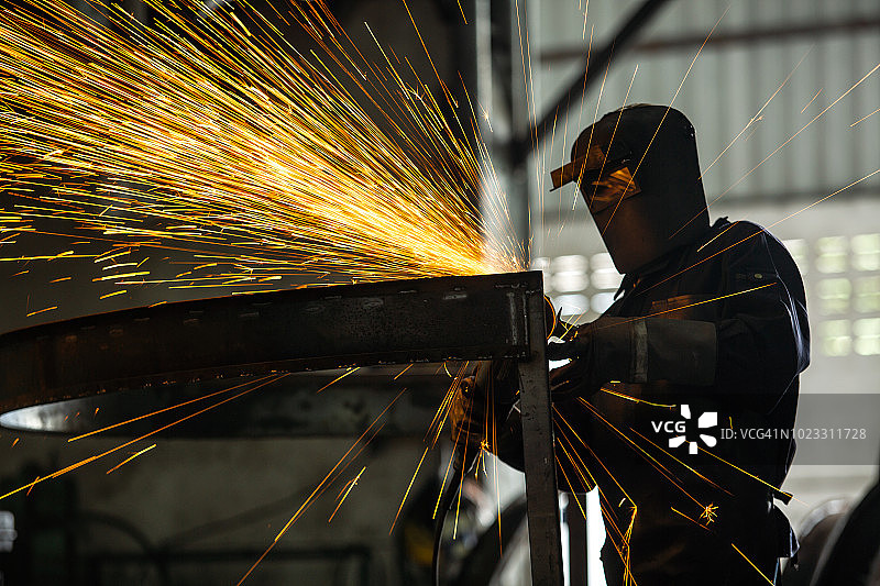 蒙面工人和安全包，电动轮在钢结构上磨削和工厂的多火花焊工。图片素材