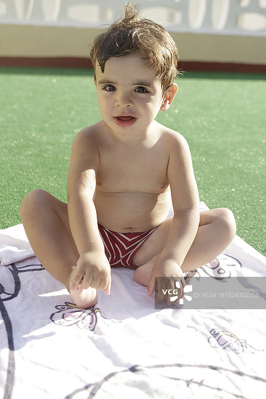 小男孩躺在泳池边的毛巾上图片素材