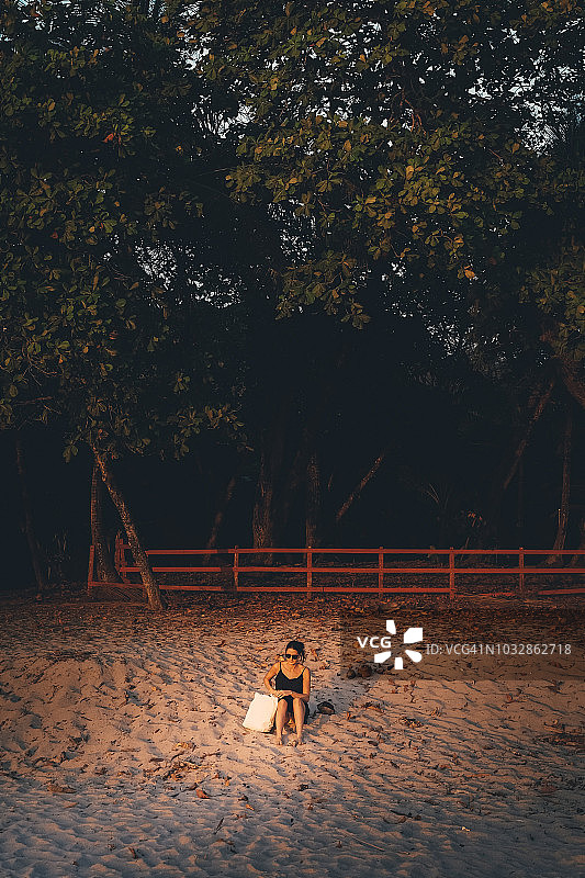 在沙滩上靠树休息的女人图片素材