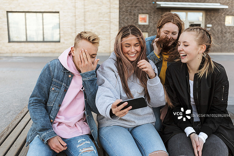 微笑的少女与朋友在城市通过智能手机自拍图片素材