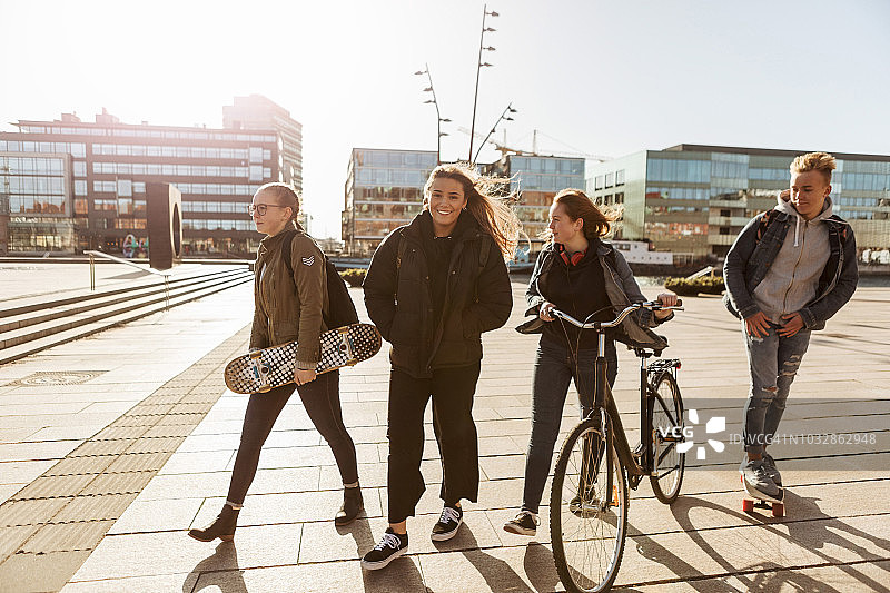 青少年朋友们骑着自行车和滑板在城市的步行区散步图片素材