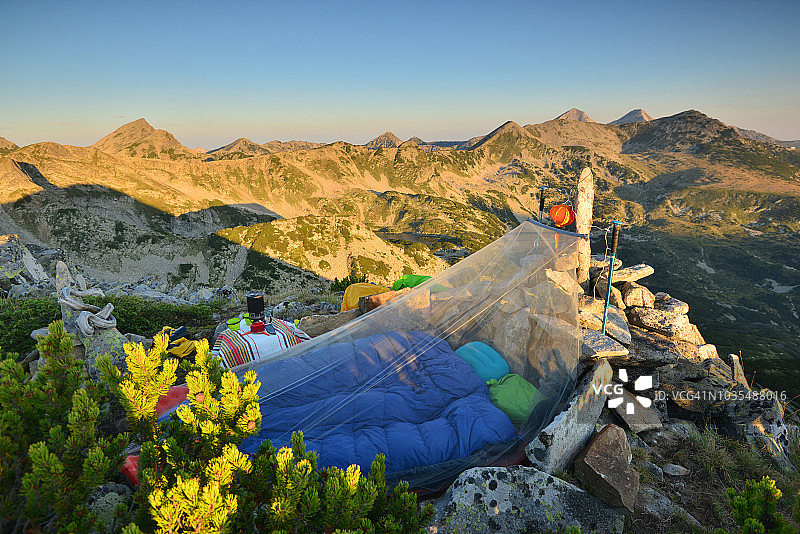 睡在星空下，日出在山顶，睡袋和蚊帐在前景图片素材
