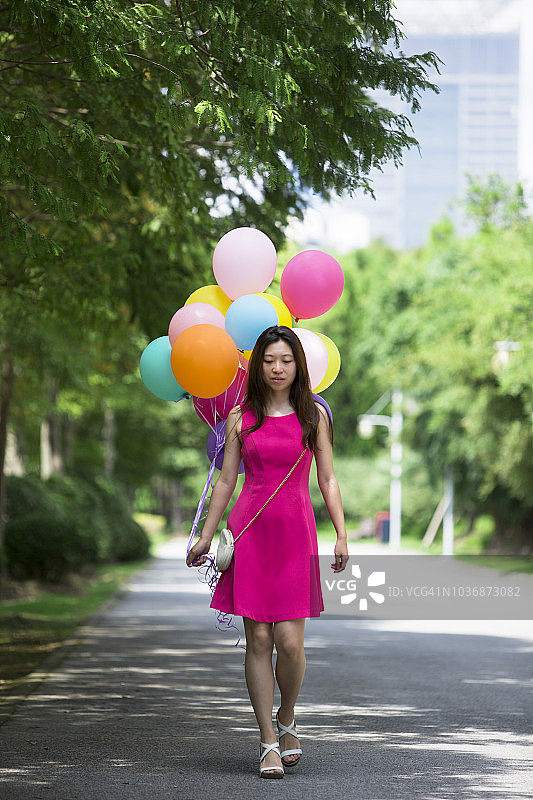 年轻的aisan女士拿着一堆彩色的气球，在公园里散步图片素材