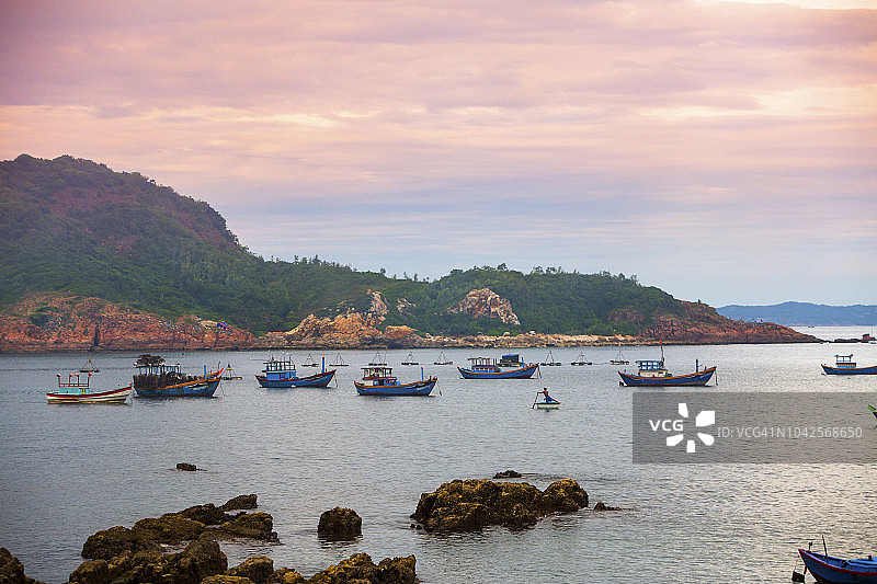 2017年6月，白赛普，越南。白溪普是一个远离旅游路线的安静偏远的渔村，距离主要城市奎Nhon 10公里。一个当地人在日落时划着他的船穿过港口。图片素材