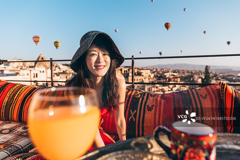 美丽的亚洲女人正在享受早餐，背景是彩色的热气球飞过卡帕多西亚的山谷，土耳其。土耳其卡帕多西亚童话般的山景。图片素材