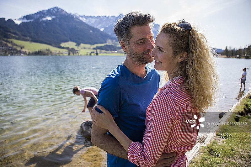 奥地利，蒂罗尔，沃奇湖，一对幸福的夫妇在湖边拥抱，背景是家人图片素材