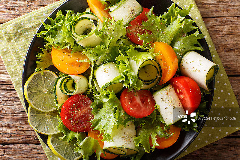 新鲜的西葫芦沙拉，西红柿，生菜和酸橙配上橄榄油，放在桌上的盘子上。水平的俯视图图片素材