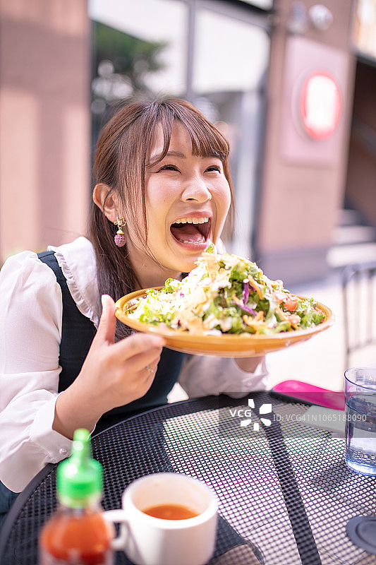 快乐的年轻女子在露天咖啡馆吃沙拉图片素材
