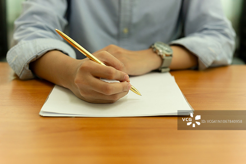 女性的手用钢笔在木桌上书写文件。图片素材
